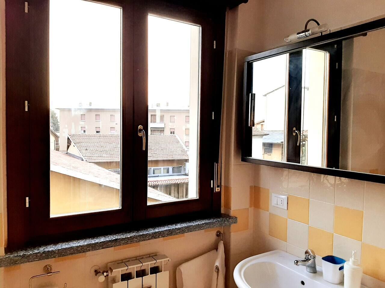 A bathroom with a window, a sink, a mirror, and a towel rack.