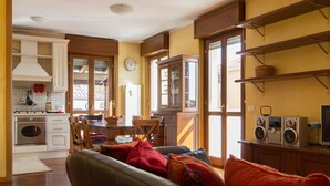 A cozy living room with a sofa, a dining area with a table and chairs, a kitchen with modern appliances, and a large window providing natural light. - Bright house with 2 bedrooms & a unique terrace (Bergamo)