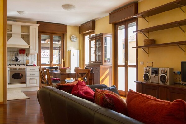 A cozy living room with a sofa, a dining area with a table and chairs, a kitchen with modern appliances, and a large window providing natural light. - Bright house with 2 bedrooms & a unique terrace (Bergamo)