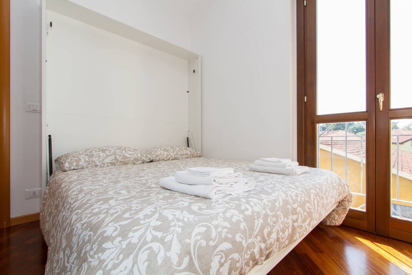 A bedroom with a bed, a large window, and a view of the outside.