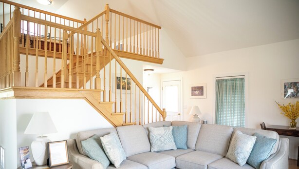 A living room with a wooden staircase, a grey sectional sofa, and a small table with a lamp.
