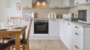 Una cocina moderna con armarios blancos, horno empotrado, microondas y una zona de comedor con una mesa y sillas de madera.