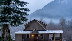 Eine Hütte mit Veranda, Kamin und Blick auf einen bewaldeten Berg.
