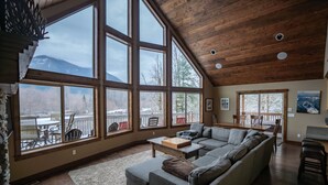 Ein geräumiges Wohnzimmer mit großen Fenstern, einer Holzbalkendecke und Bergblick.