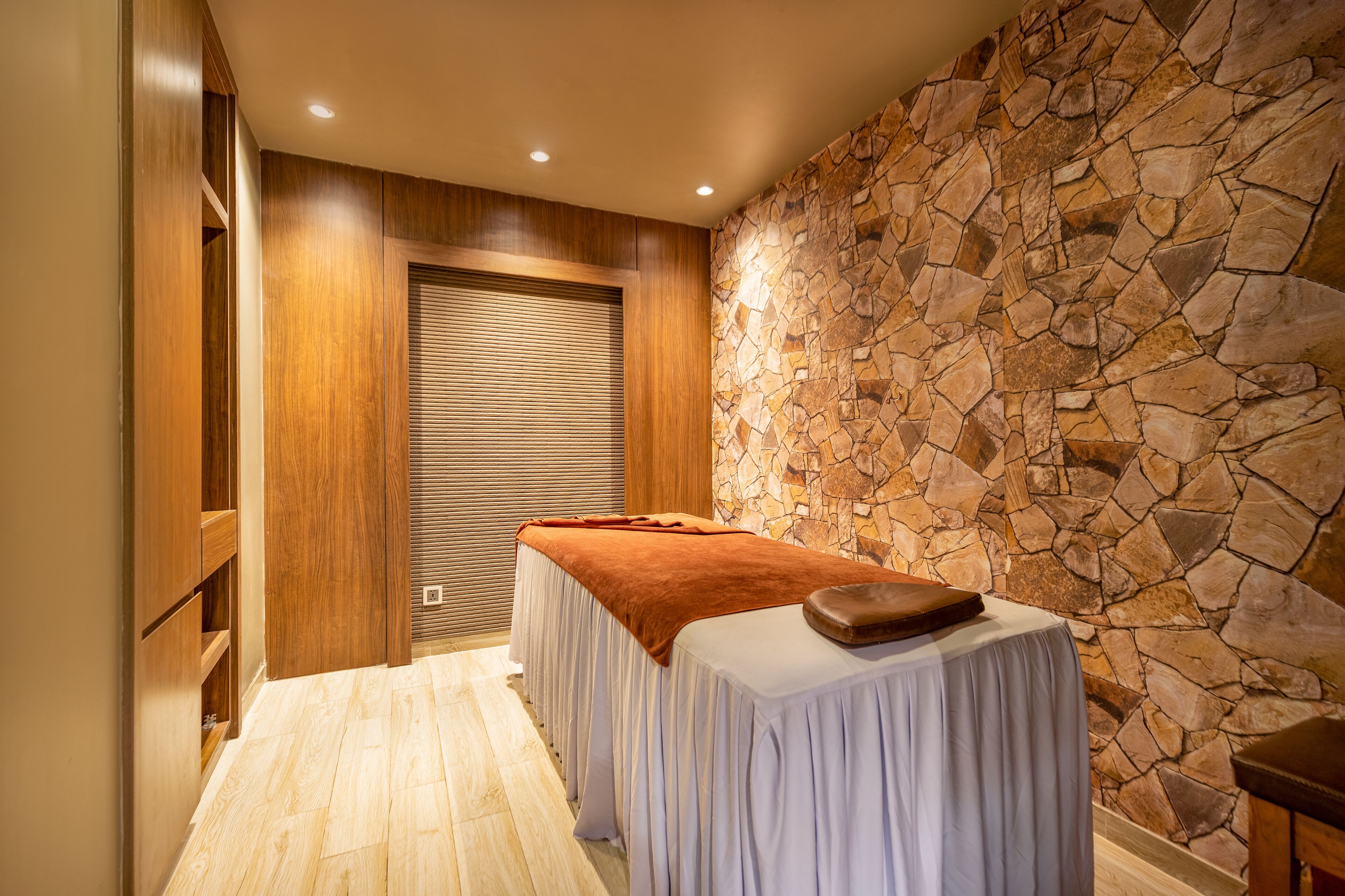 A spa room with a massage table, wooden paneling, and a stone wall.