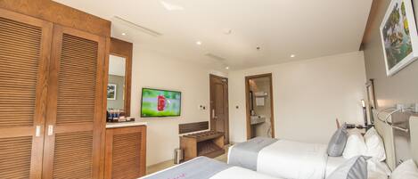 A hotel room with two beds, a wooden wardrobe, a television, and a bathroom visible through an open door.