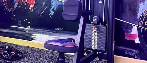 A gym with a squat rack, bench press, and a wall with a colorful mural.