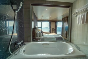 A modern bathroom with a large bathtub, a shower, and a view of a bedroom with a bed and a view of the mountains. - Cat ba Paradise Hotel (Hai Phong)