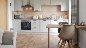 A modern kitchen with white cabinets, a microwave, toaster, and kettle. There's a dining area with a table and chairs. - Rockworks Chalets No.3 - UK7042 (Holm, near Kirkwall)