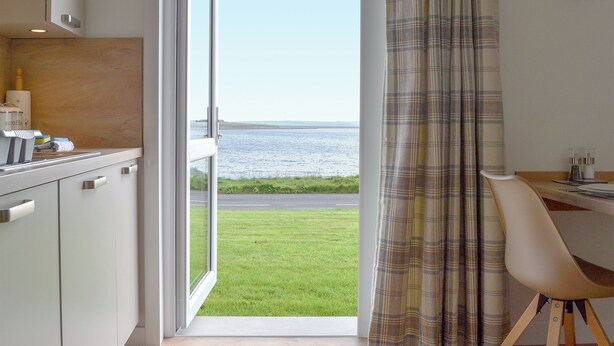 A room with a view of the sea, a dining area, and a kitchen. - Rockworks Chalets No.3 - UK7042 (Holm, near Kirkwall)