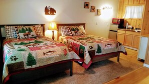A bedroom with two beds, a nightstand, a lamp, a refrigerator, and a wooden cabinet.