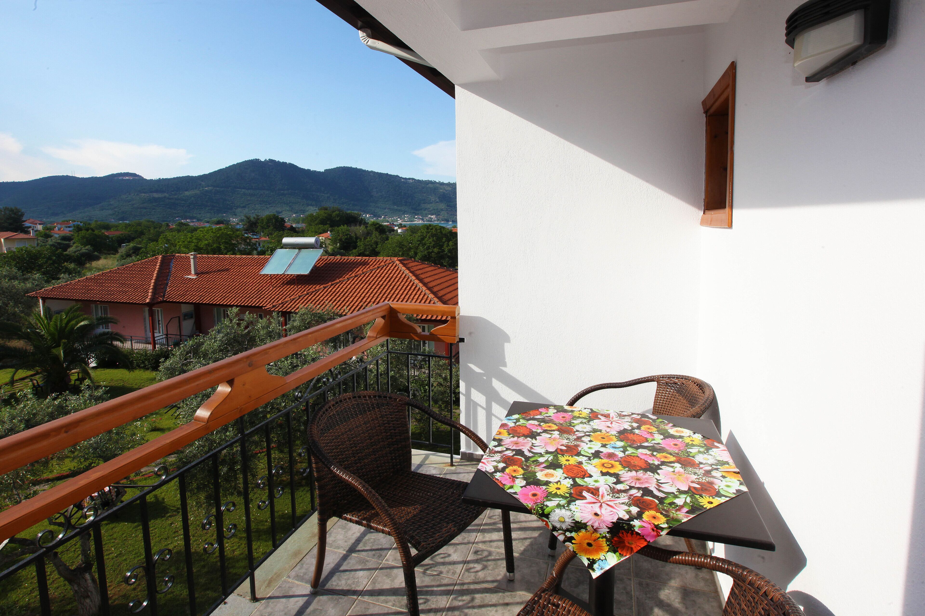 Un balcón con sillas de mimbre y una mesa, con vistas a un paisaje montañoso.