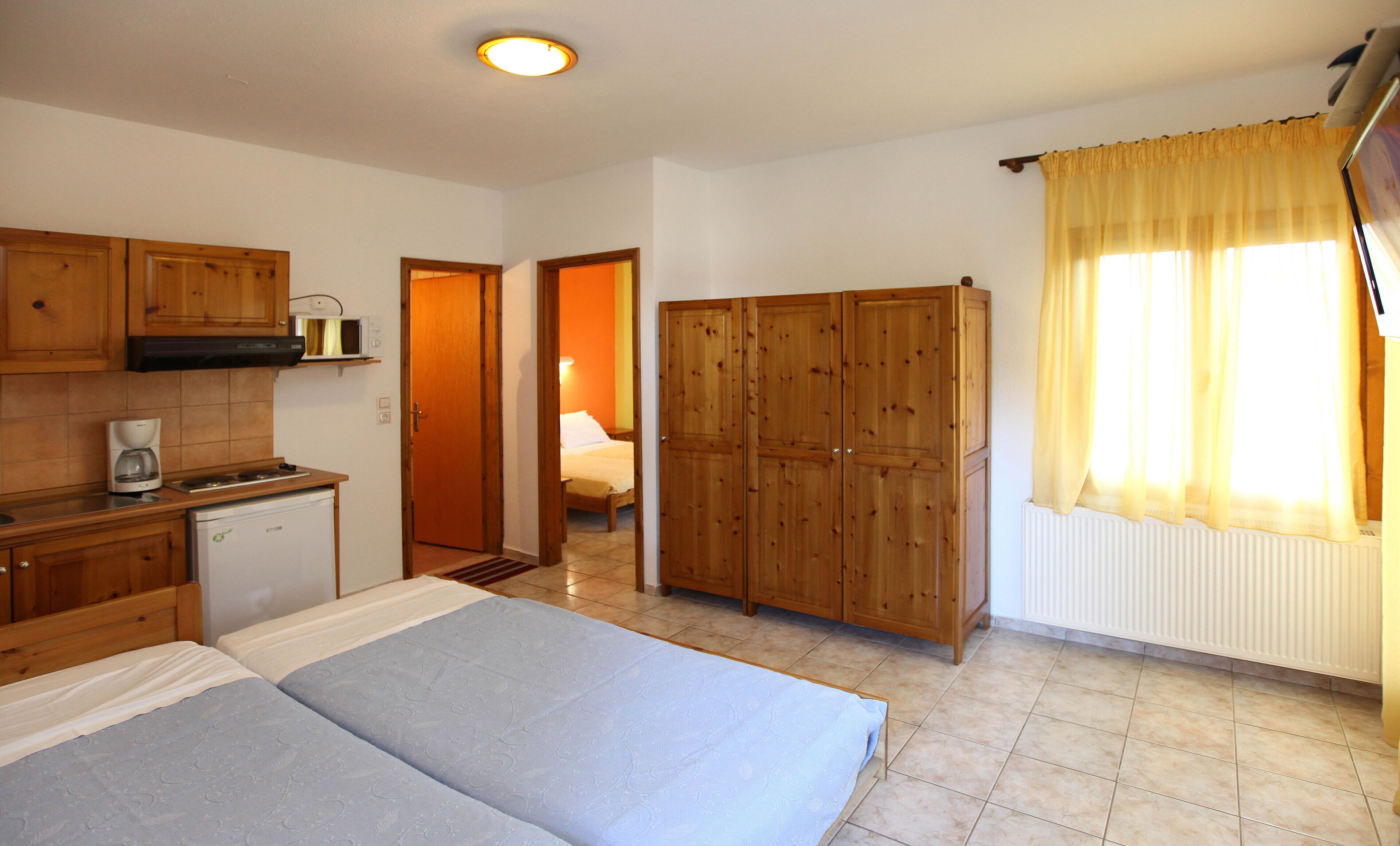 A bedroom with a bed, a wardrobe, a kitchenette, and a bathroom.