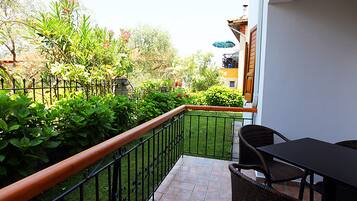 A balcony with a table and chairs, surrounded by greenery and a fence.