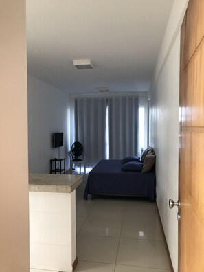 A narrow room with a bed, a TV, and a fan.