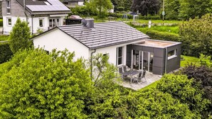 Una casa moderna con pannelli solari, un giardino e un piccolo spazio esterno con posti a sedere.