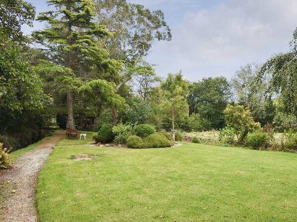 Un jardin bien entretenu, agrémenté de divers arbres et arbustes, d’un chemin de gravier et d’un banc en bois.