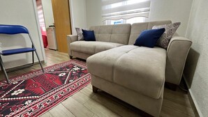 A living room with a beige sofa, blue cushions, a patterned rug, and a blue folding chair. - No:85 Konaklama Tesisi (Marmaris)