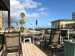 A wooden deck with outdoor seating, a stop sign, and a building with a sign reading "Sandy Shores". - 1 Bedroom / 1st floor Beachside House (Jacksonville Beach)