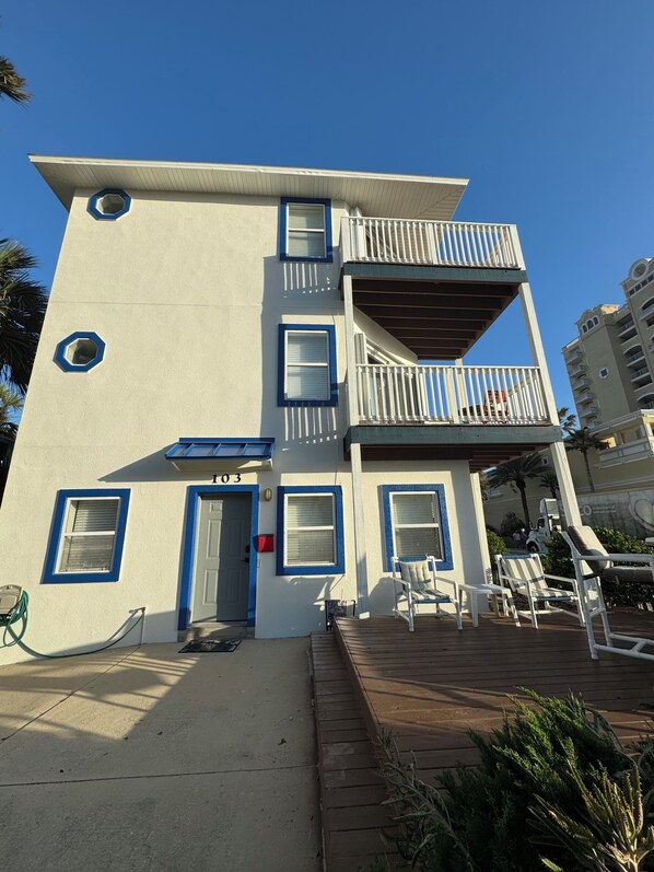 A two-story building with a balcony on the second floor, a door with a number '103' on it, and a small deck area with chairs. - 1 Bedroom / 1st floor Beachside House (Jacksonville Beach)