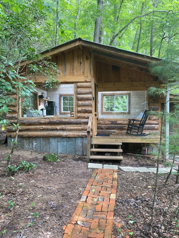 A rustic log cabin with a porch, a fireplace, and a brick pathway leading to the entrance. - The Moon and You-
Unique creek side off grid 1-bedroom cabin with glass roof (Purlear)