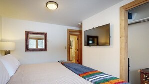 A bedroom with a bed, a TV mounted on the wall, a window, and a door. - COMFY COZY SLOPESIDE CONDO-HOT TUB HEATED POOL ACCESS -5 MIN FREE RIDE TO LIFTS (Teton Village)