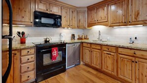 A kitchen with wooden cabinets, a black stove, a microwave, and a dishwasher. - COMFY COZY SLOPESIDE CONDO-HOT TUB HEATED POOL ACCESS -5 MIN FREE RIDE TO LIFTS (Teton Village)