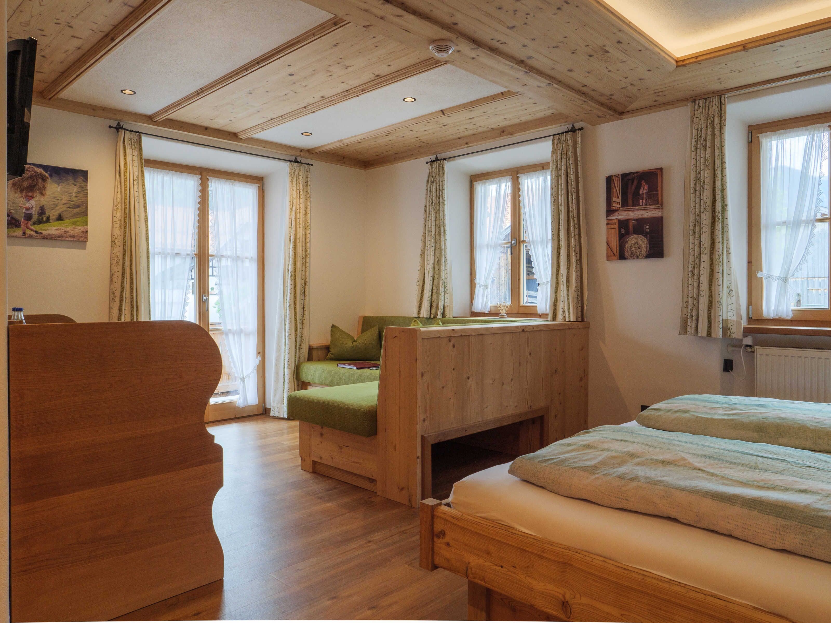A wooden room with a bed, a chair, and a window with curtains.