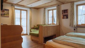 A wooden room with a bed, a chair, and a window with curtains.