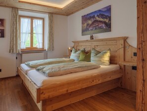 Una cama de madera con cabecera, una ventana con cortinas y un cuadro de un paisaje montañoso en la pared.