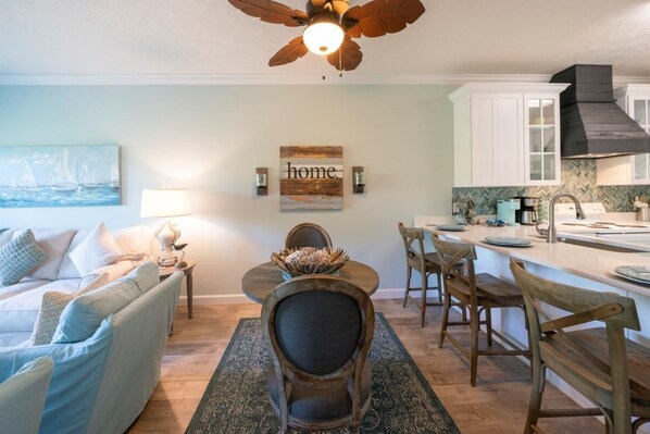 A modern kitchen with white cabinets, a black range hood, and a dining area with wooden chairs and a round table. - Sun, Sand & 30A: Your Perfect July Stay Awaits. 3 Bikes included (Santa Rosa Beach)