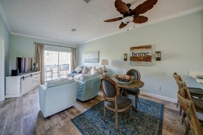 A cozy living room with a sofa, dining table, and chairs, a ceiling fan, and a view through a window.