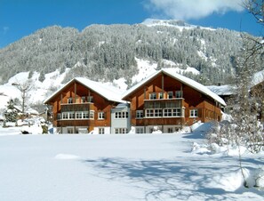 Uma cabana de madeira com telhado coberto de neve, emoldurada por montanhas.