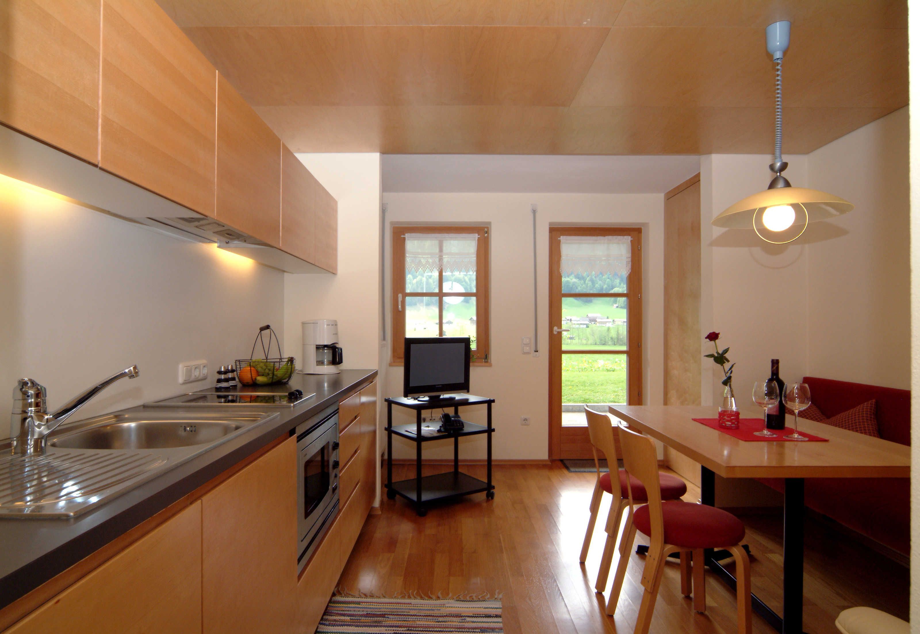 A kitchen with a built-in oven, a sink, a dining area with a table and chairs, and a TV on a stand.