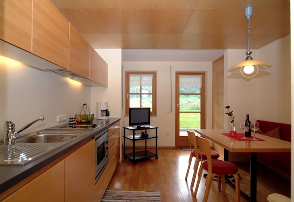 A kitchen with a built-in oven, a sink, a dining area with a table and chairs, and a TV on a stand.