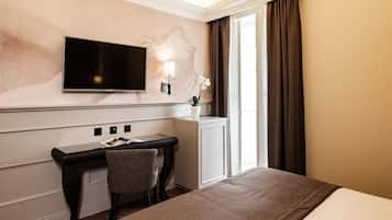 Une chambre d’hôtel comprenant un lit, un bureau avec une chaise, un téléviseur à écran plat fixé au mur, un petit placard et une fenêtre avec des rideaux.