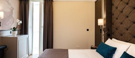 A hotel room with a large bed, a desk with a lamp, a small cabinet, and a mirror on the wall.