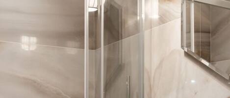Une salle de bain moderne dotée d’une douche à parois de verre, d’un mur recouvert de carreaux de marbre, d’un lavabo avec un receveur en pierre et de deux appliques murales.