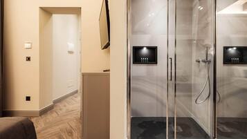 A modern bathroom with a glass shower enclosure, a vanity with a mirror, and a small shelf with toiletries.