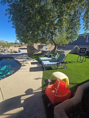 A backyard with a swimming pool, lounge chairs, a small orange toy car, and a target on a stand. - Relaxing country style home with spacious backyard in a quiet neighborhood. (Peoria)