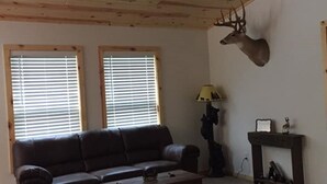 A living room with a wooden ceiling, two windows with blinds, a black sofa, a coffee table, a lamp, and a mounted deer head. - LOCATION - LOCATION -- SNOWMOBILING, ICE FISHING & MUCH MORE, - GREAT GETAWAY (Minocqua)