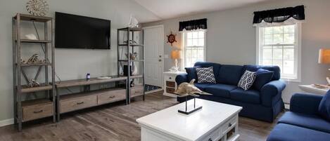 A living room with a blue sofa, white coffee table, and a TV mounted on the wall.
