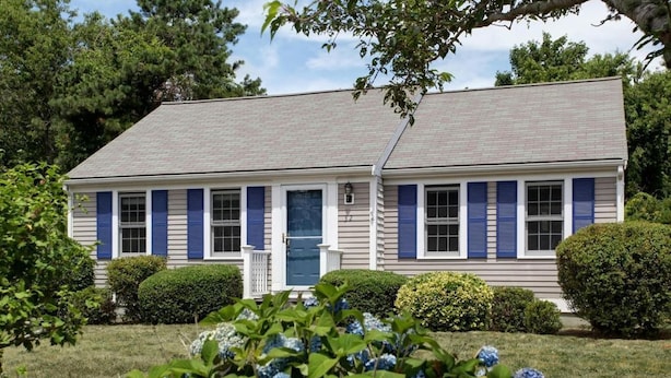 A two-story house with a front porch, blue shutters, and a well-maintained lawn with hydrangea bushes.