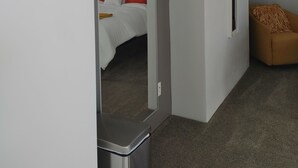 Una habitación de hotel moderna con un espejo grande, una cama con ropa de cama naranja y blanca, un pequeño sofá y un cuadro en la pared.