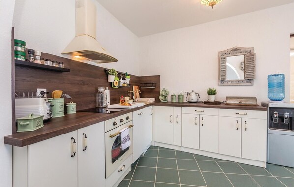 A kitchen with white cabinets, a stove, and a sink. There are various kitchen items on the counter, including jars and a kettle. - Cozy home in Josinovac with sauna (Josinovac)