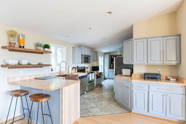 A modern kitchen with grey cabinets, a central island with stools, and a microwave above the sink. - Tenmile Lakeview Hideaway (Lakeside)