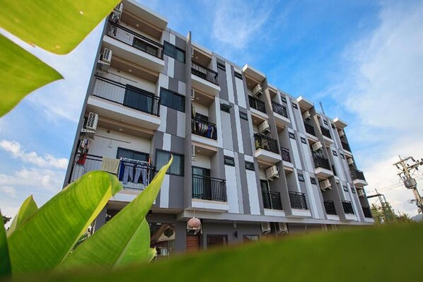 A multi-story residential building with balconies, air conditioning units, and a clear sky. - Be Live Residence (Thep Krasattri)