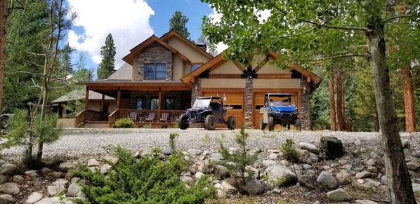 Un chalet à la façade en pierre, doté d’un porche abrité et où sont garés deux véhicules tout-terrain devant l’entrée.