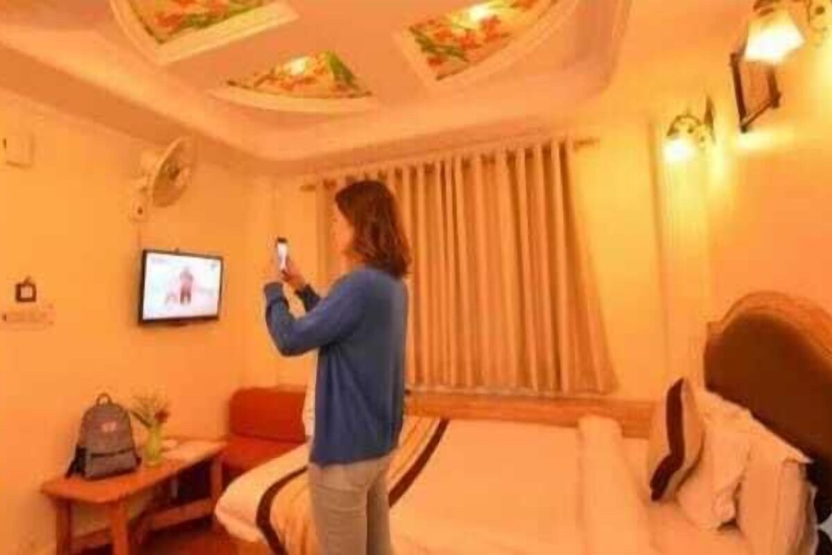 A hotel room with a bed, a TV, a desk with a laptop, and a window with curtains.