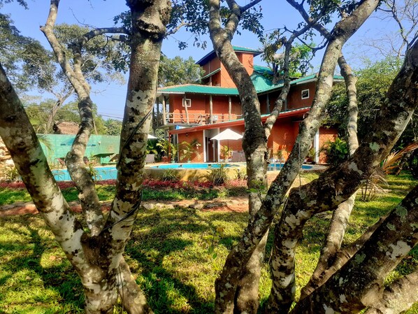 A two-story building with a red exterior and green roof, surrounded by trees and a swimming pool. - Sigiri Heritage Villa (Sigiriya)